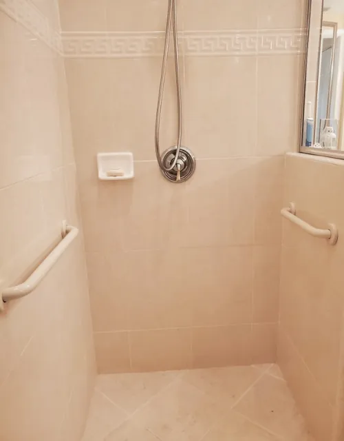 Pair of white grab bars in a tiled shower with handheld shower